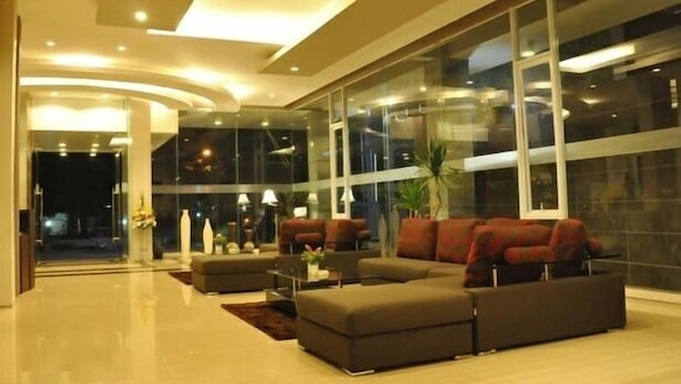 A modern living room with a sectional sofa, a coffee table, and a large window offering a view of the night outside. - Andelir Hotel (Bandung)