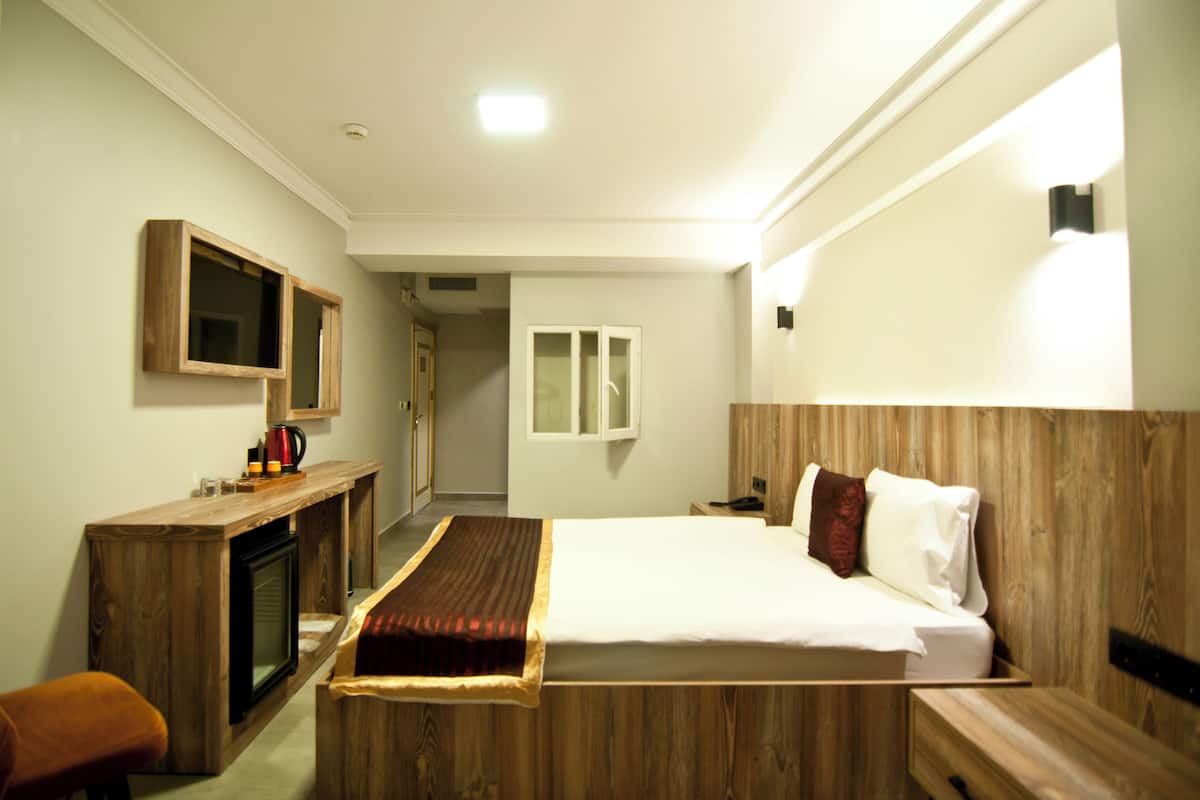 A hotel room with a wooden bed, a desk with a television, and a small seating area.