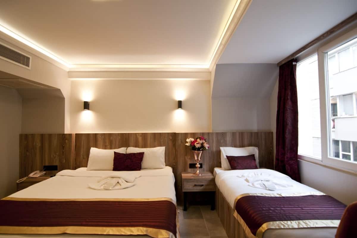 A hotel room with two beds, a nightstand with a phone, a vase with flowers, and a window with curtains.