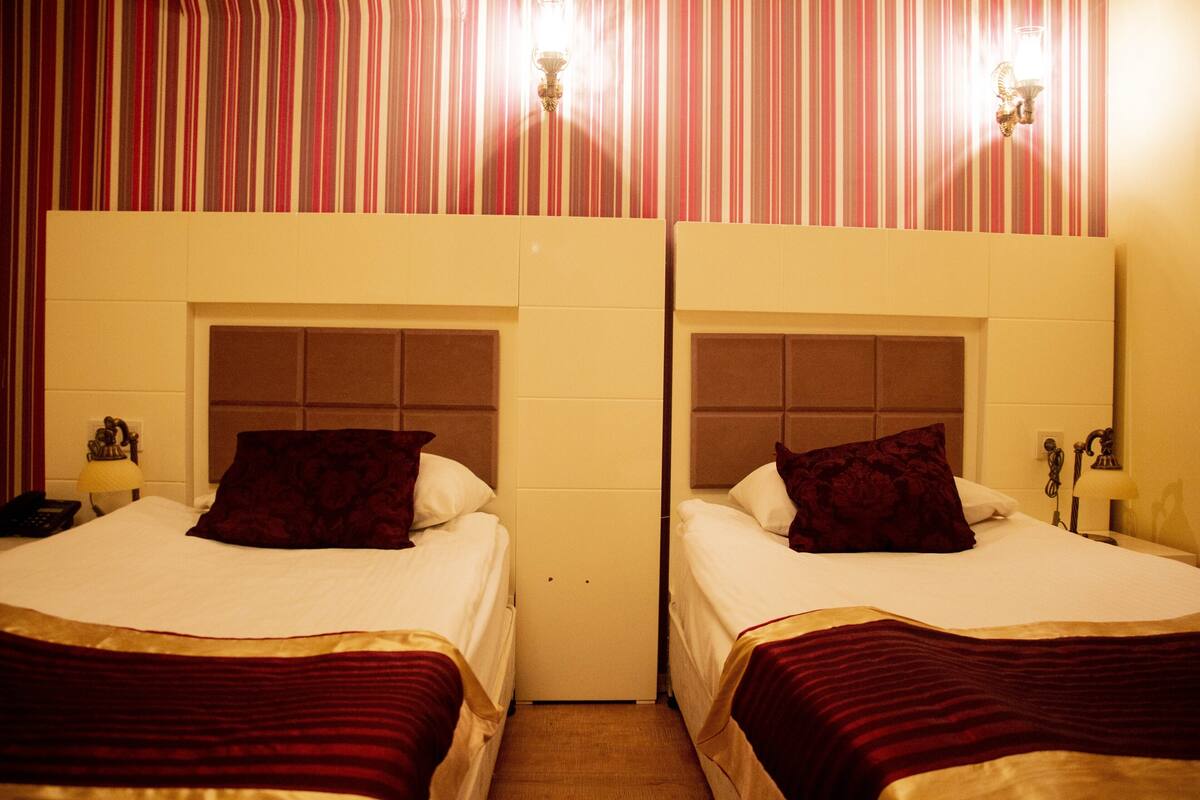 Two twin beds with headboards, a striped wall, and a small bedside table with a lamp.