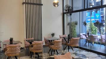 Un intérieur moderne avec différents types d’assises, notamment des tables et des chaises, un luminaire décoratif et une grande fenêtre donnant sur la rue.