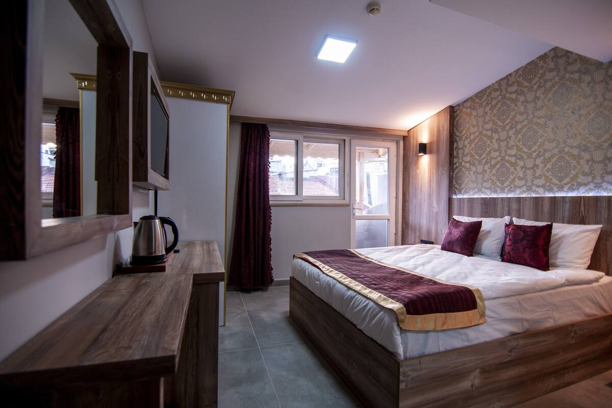 A bedroom with a wooden bed, a bedside table, a mirror, and a window with curtains.