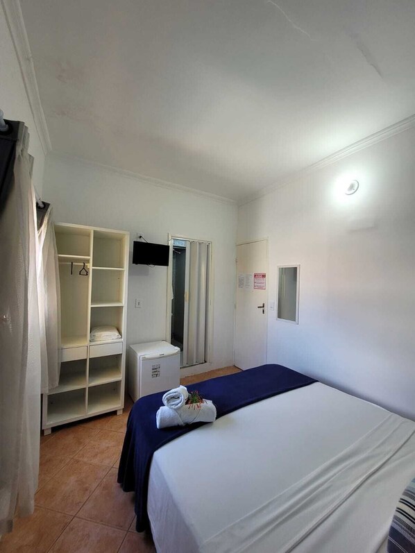 Una habitación de hotel con cama, armario, escritorio y ducha.