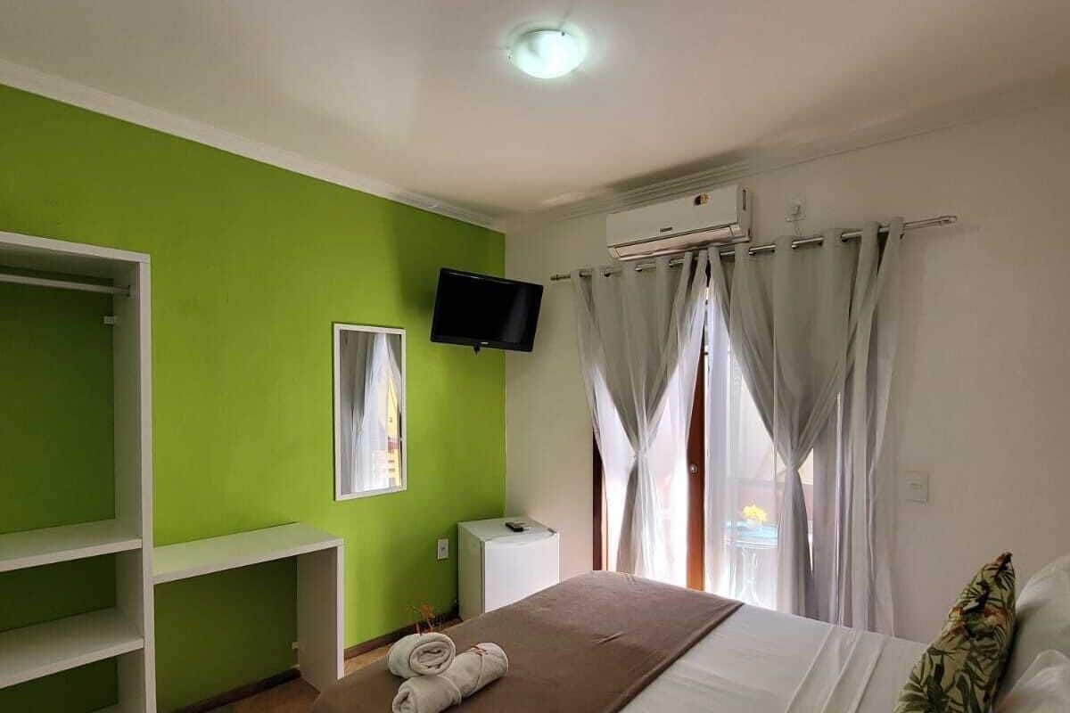 A hotel room with a bed, a TV, a wardrobe, and a window with curtains.