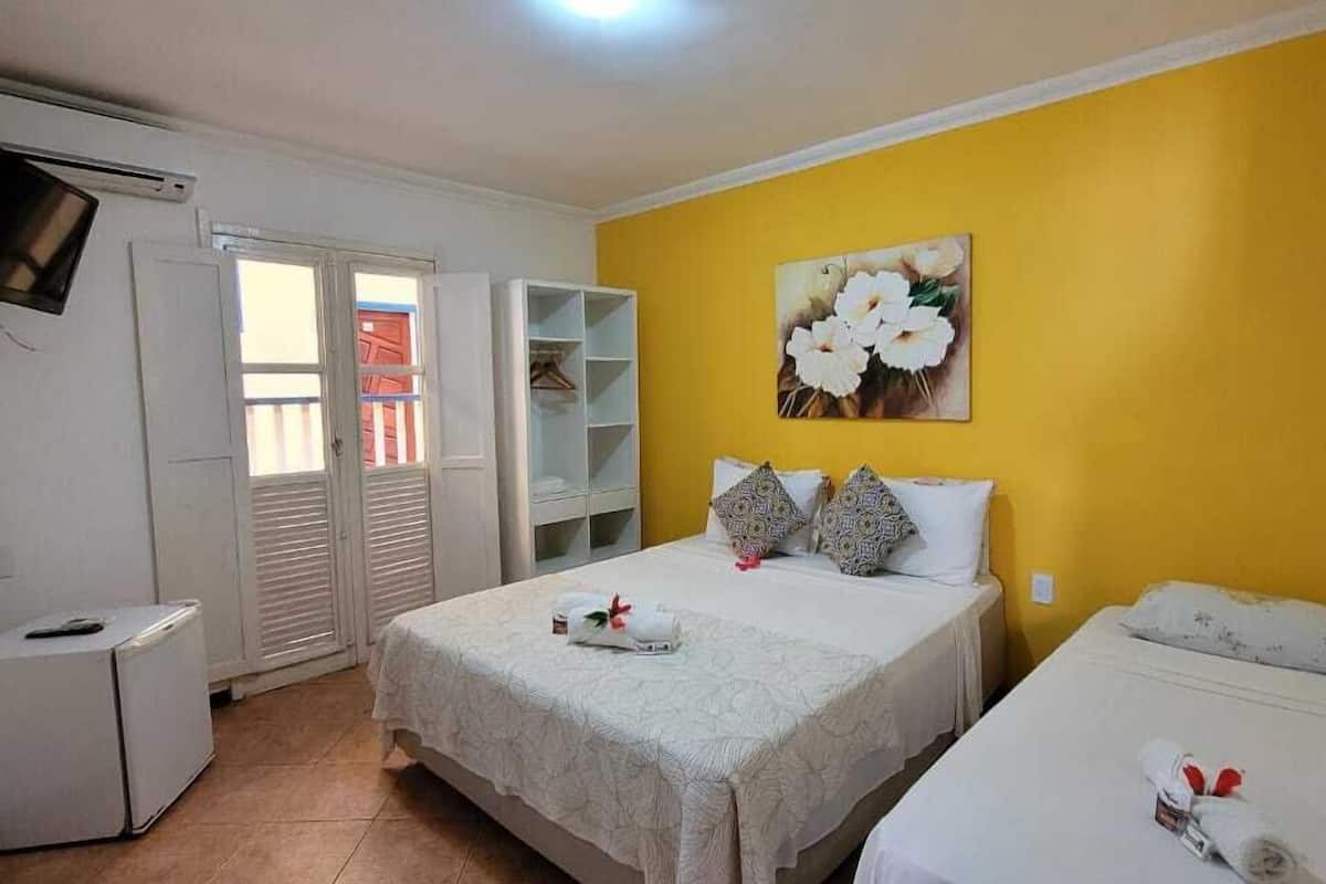 A hotel room with two beds, a TV, a wardrobe, and a painting on the wall.
