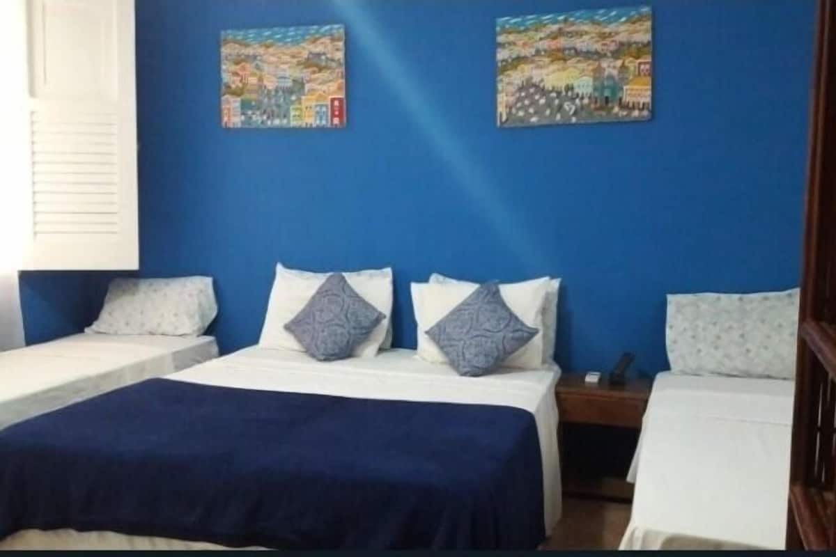 A room with two beds, a blue wall, and two paintings.