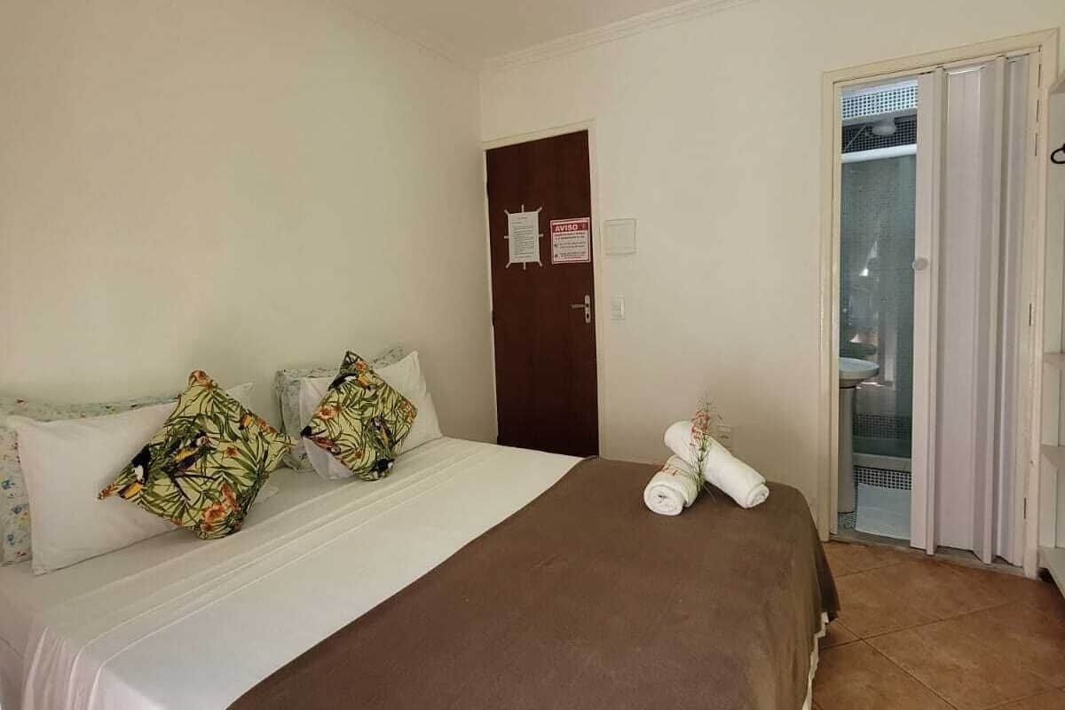 A hotel room with a bed, a brown blanket, a towel, and a door with a sign.