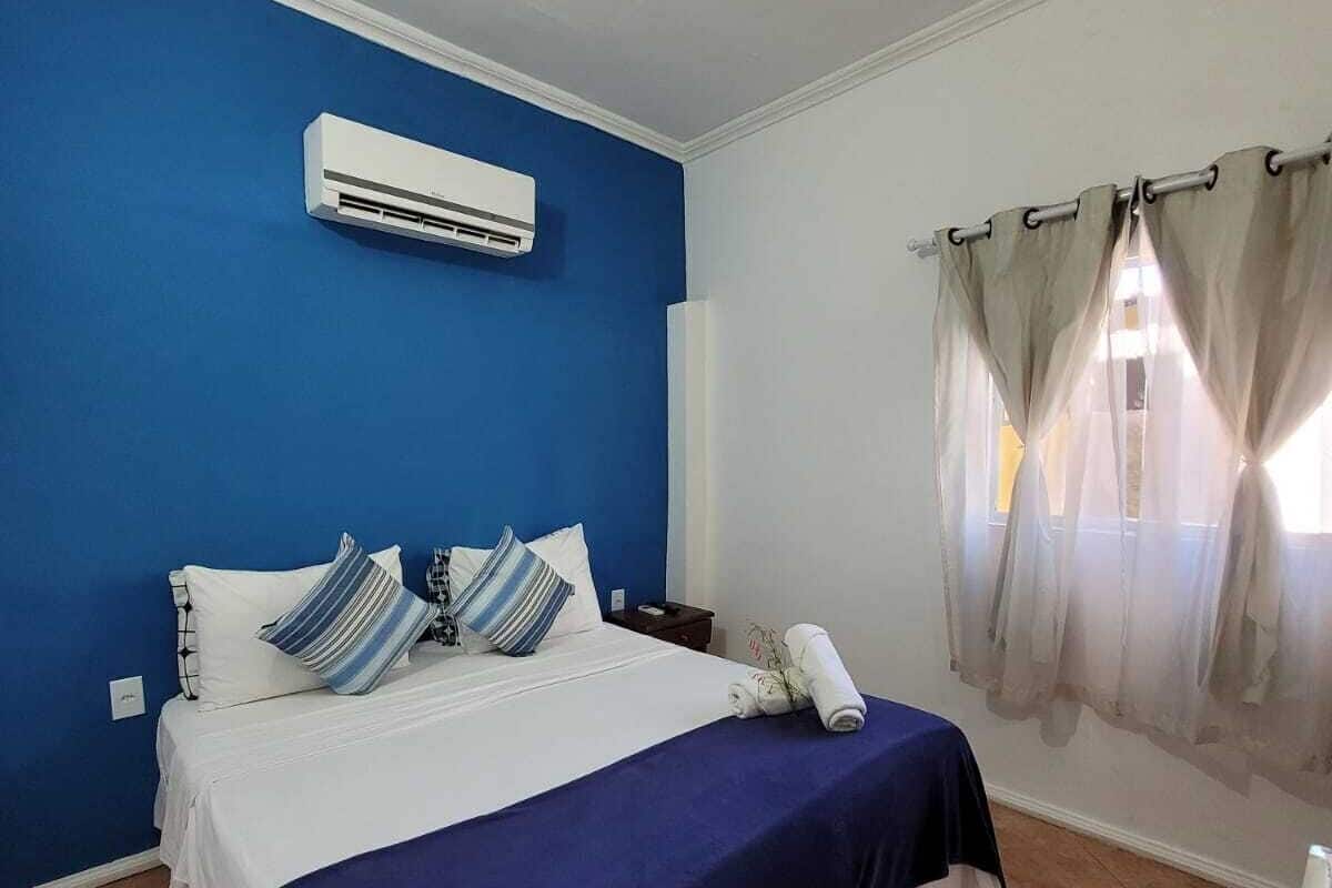 A bedroom with a bed, an air conditioner, a nightstand, a lamp, and a window with curtains.