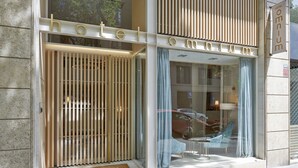 A hotel entrance with a modern design, featuring a glass door with vertical blinds, a visible reception desk, and a clear view of the street outside. - Hotel Omnium (Barcelona)