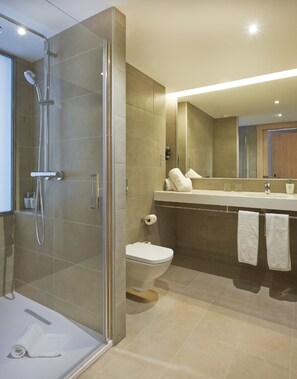 A modern bathroom with a glass-enclosed shower, a toilet, and a vanity with a mirror. - Hotel Omnium (Barcelona)