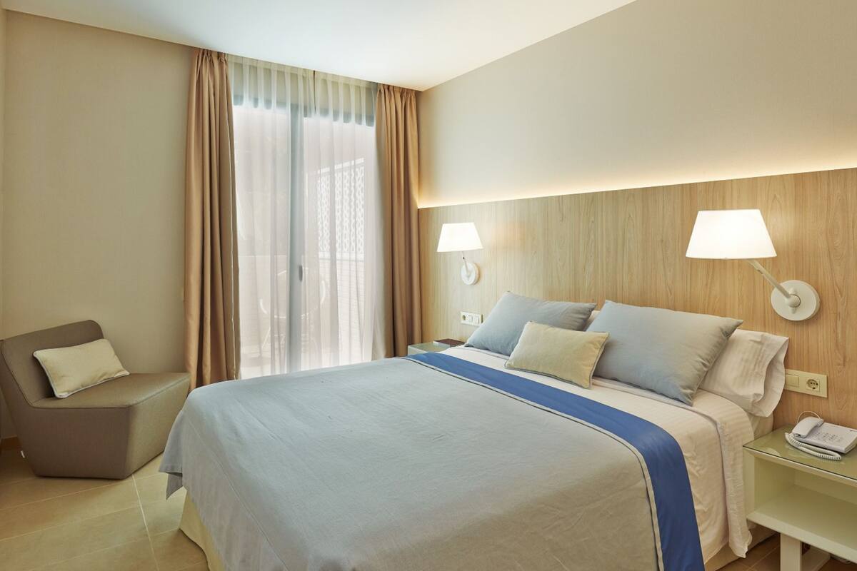Habitación de hotel con cama, lámparas de noche, una silla y un escritorio con teléfono.