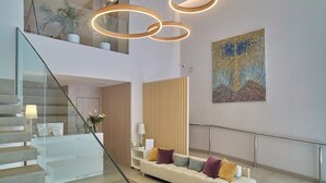 A modern interior with a staircase, a white sofa with cushions, a wooden panel wall, and a painting. - Hotel Omnium (Barcelona)