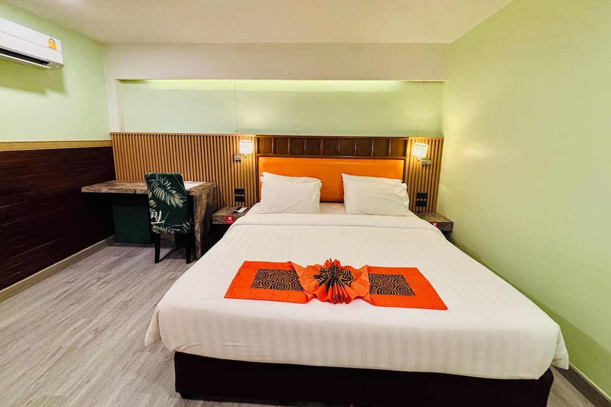 A hotel room with a bed, bedside tables, a chair, and an air conditioning unit.