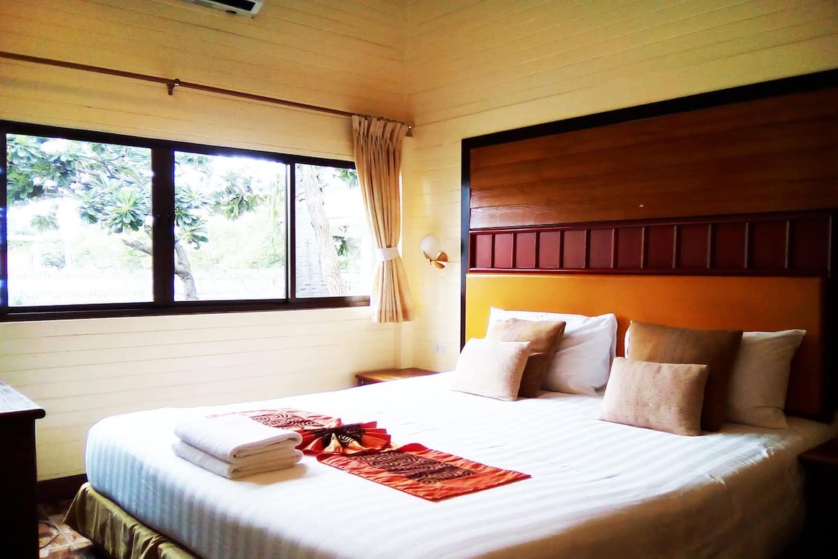A hotel room with a bed, a window with curtains, a wooden headboard, and a nightstand.