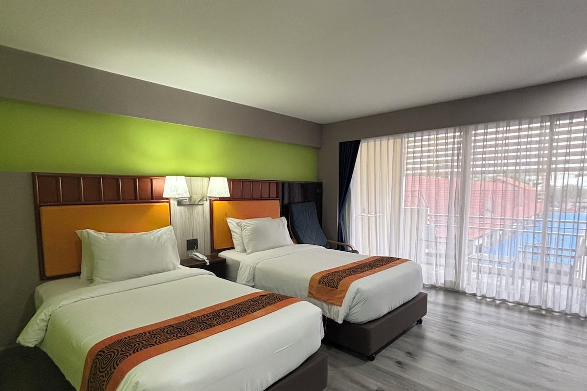A hotel room with two beds, a nightstand, a lamp, and a large window with blinds.