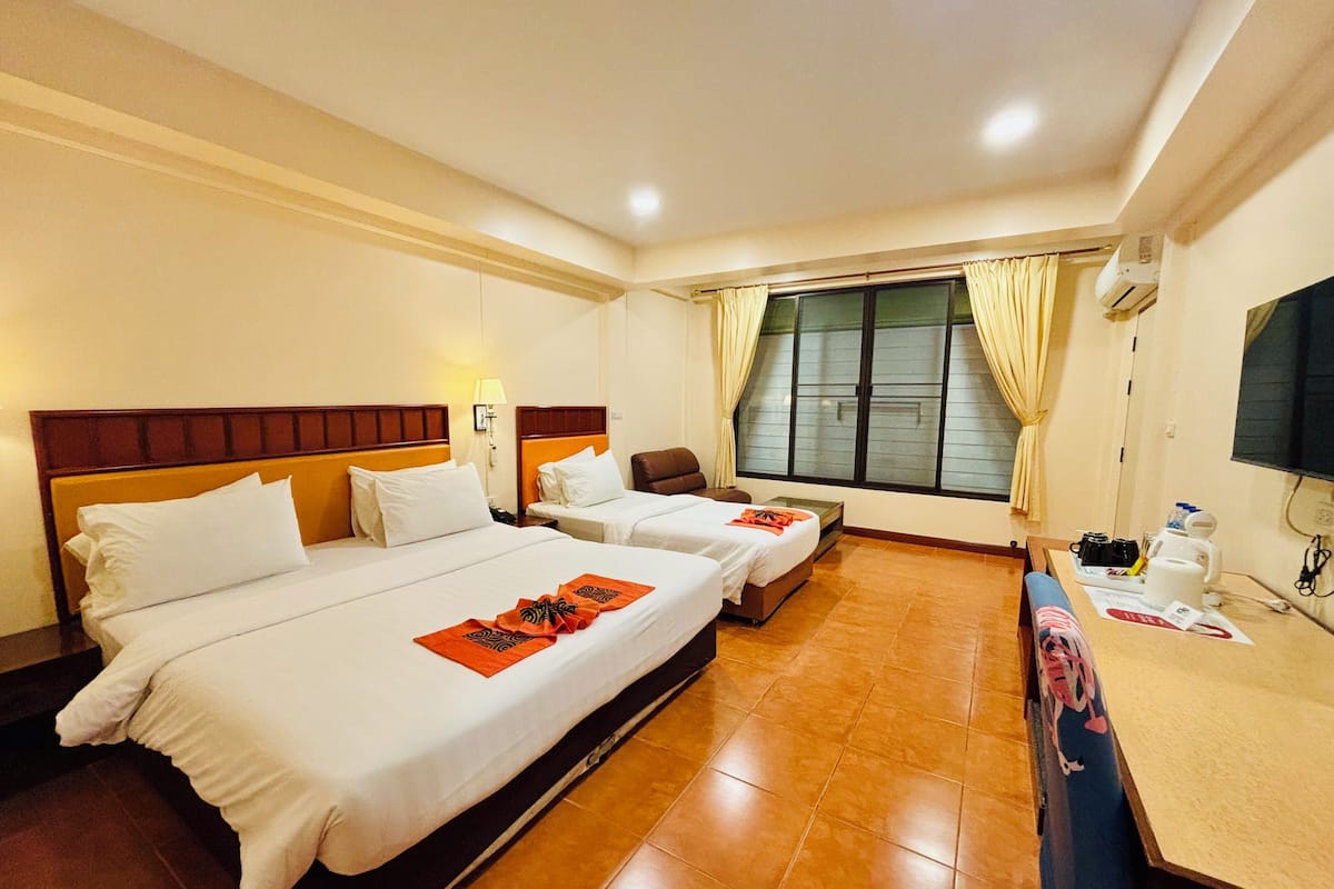 A hotel room with two beds, a desk, a chair, a window with curtains, and a television.