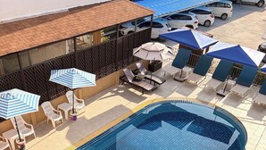 Una piscina con suelo de baldosas, rodeada de sillones de playa y sombrillas.