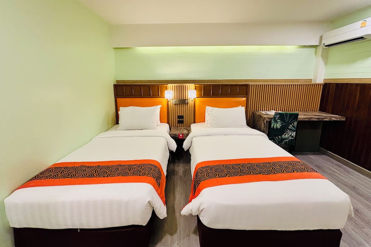 A hotel room with two beds, a wooden headboard, a nightstand, and a table with a plant.