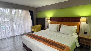 Una habitación de hotel con una cama grande, piso de madera, una pared de acento verde y vistas a través de un ventanal amplio.