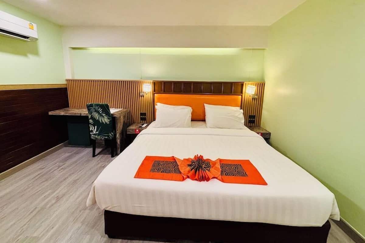 A hotel room with a bed, bedside tables, a chair, and an air conditioning unit.