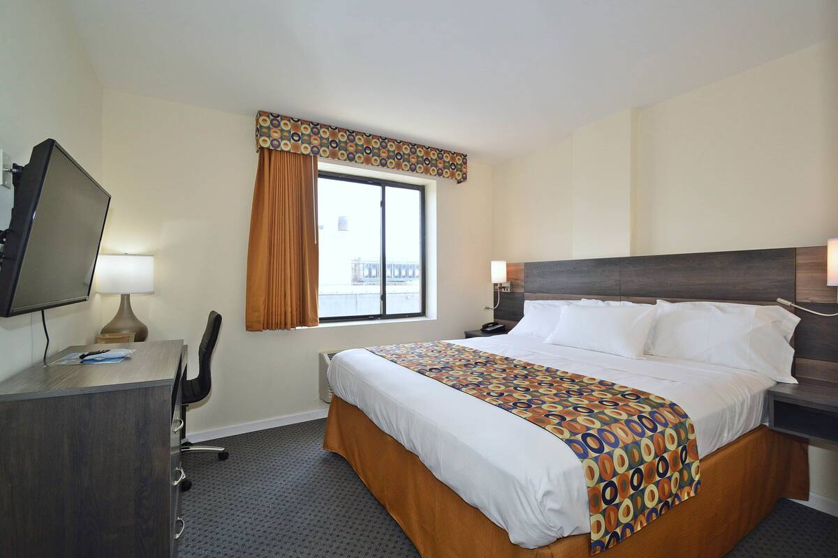 A hotel room with a bed, desk, chair, TV, and window with curtains.