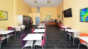 En kantine med borde, stole, et køleskab og kaffestation.