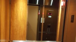 Elevatorinteriør med træpaneler og et metallisk kontrolpanel.