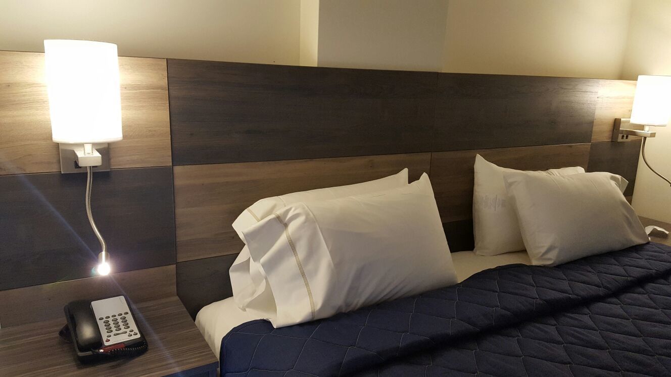 A hotel room with a bed, two bedside lamps, a telephone, and a dark-colored quilt.