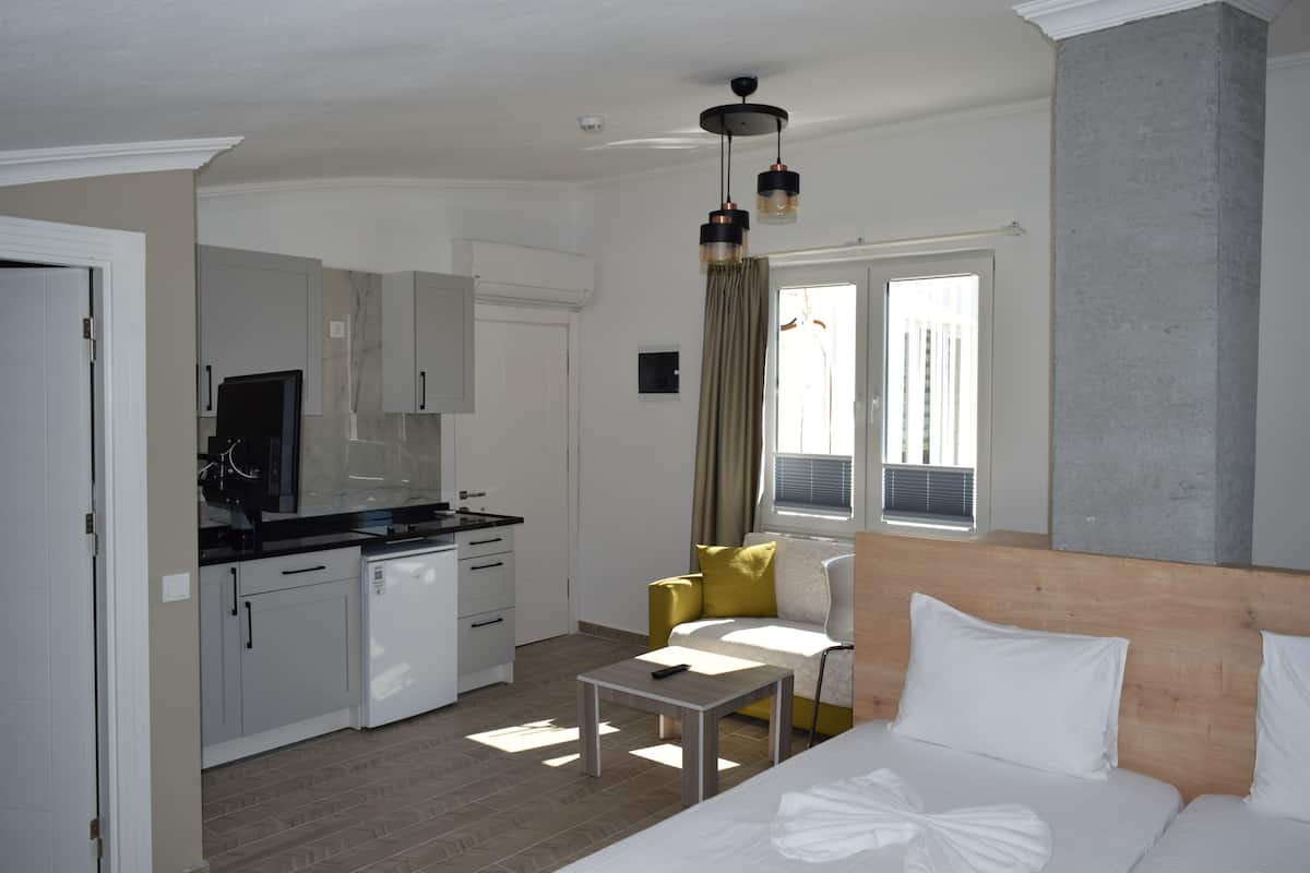 Een moderne hotelkamer met een bed, een tafeltje, een bank, een kitchenette en een raam met gordijnen.