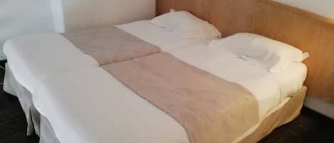 A double bed with white and beige bedding, a wooden headboard, and a small blue object on a white shelf above.