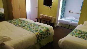 A hotel room with two beds, a wooden wardrobe, a radiator, and a television on the wall.