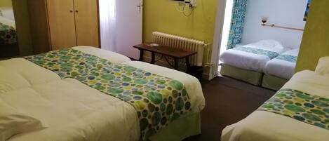 A hotel room with two beds, a wooden wardrobe, a radiator, and a television on the wall.