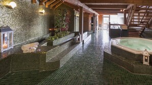 A spa area with a hot tub, tiled walls, wooden beams, and a staircase. - Hotel Serena (Badia)