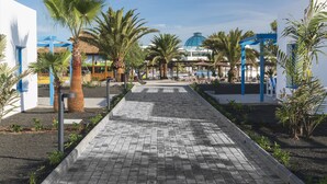 Un camí pavimentat flanquejat per palmeres i una construcció blava al fons.