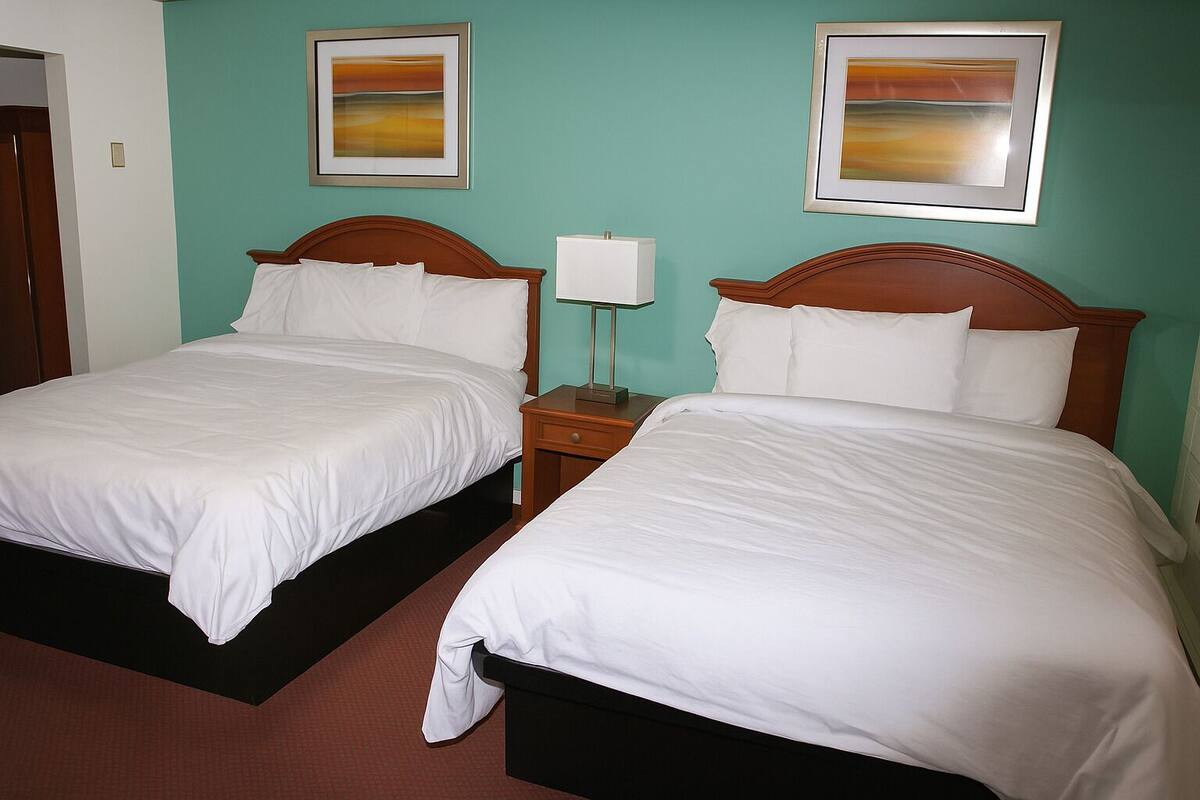A hotel room with two beds, a nightstand with a lamp, and two framed pictures on the wall.