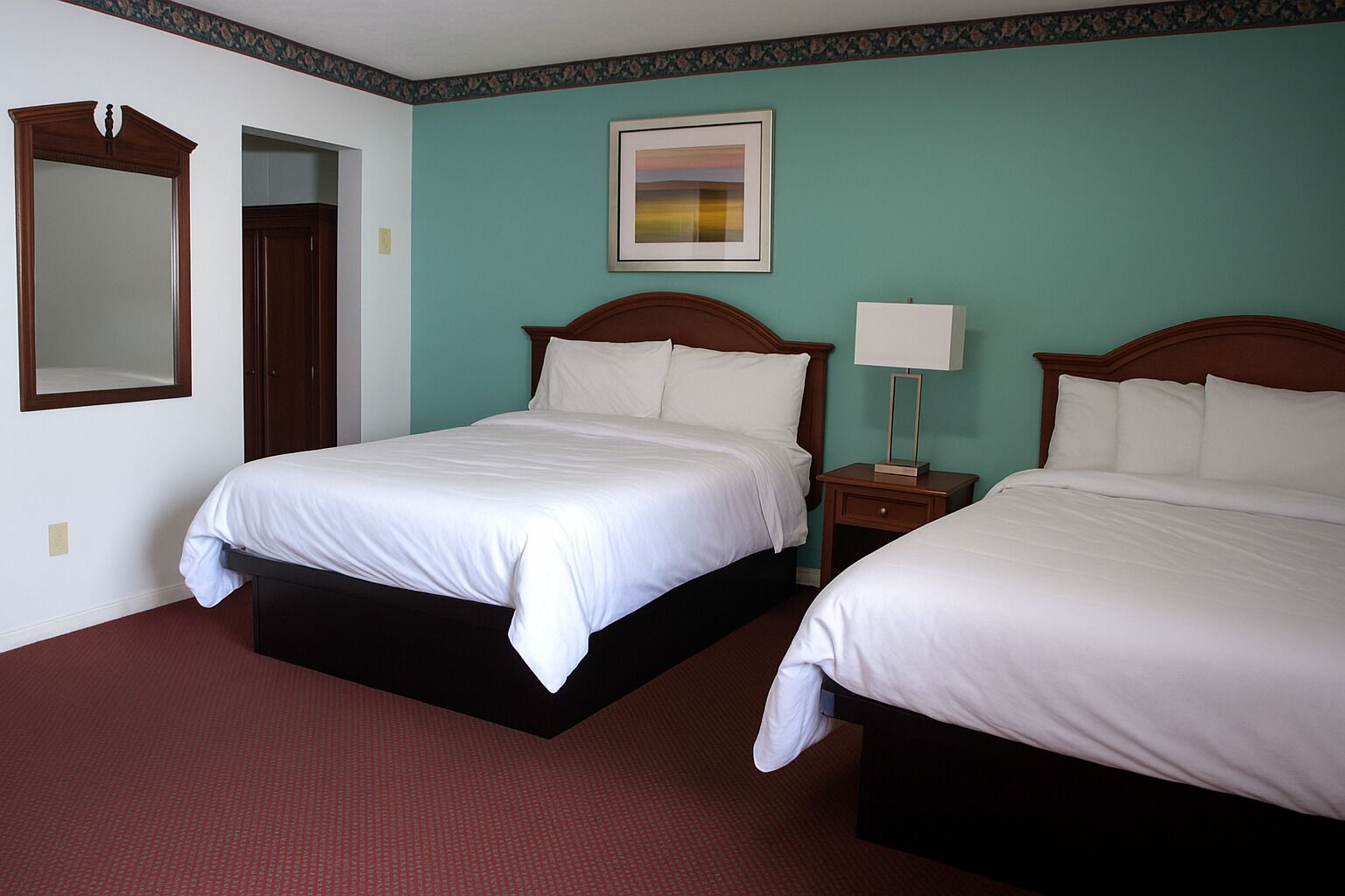 Habitación de hotel con dos camas, una mesita de noche con lámpara, un cuadro enmarcado en la pared y un espejo sobre la puerta.