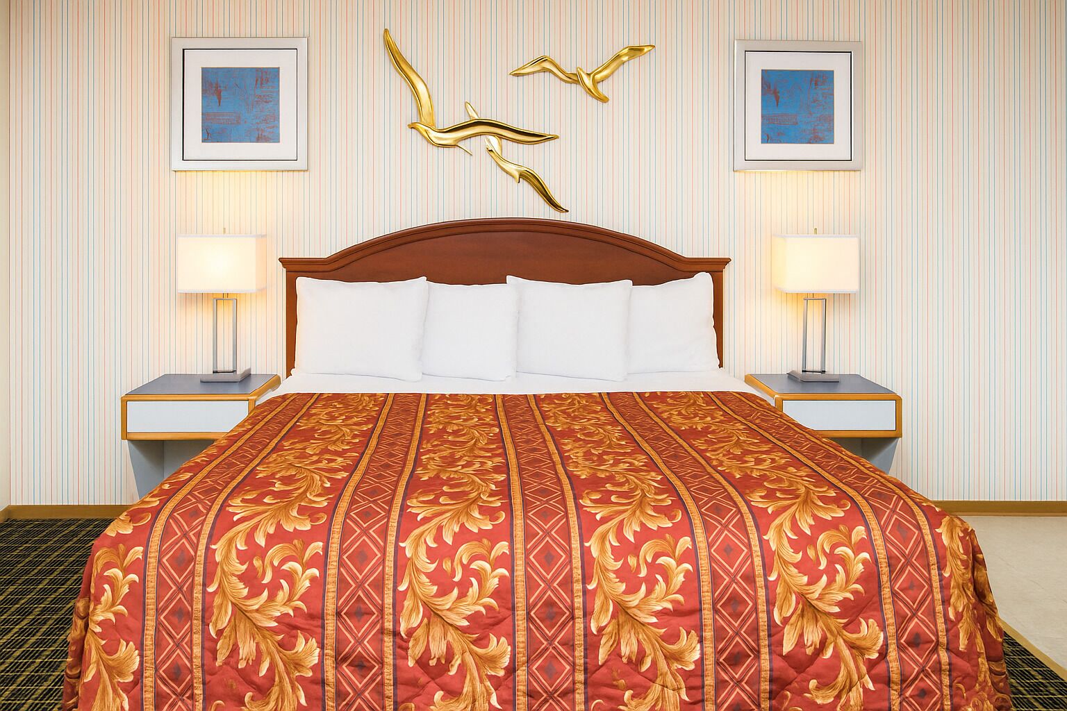 Une chambre d’hôtel avec un grand lit, deux tables de chevet et un mur recouvert d’un papier peint à rayures et orné d’œuvres d’art encadrées.