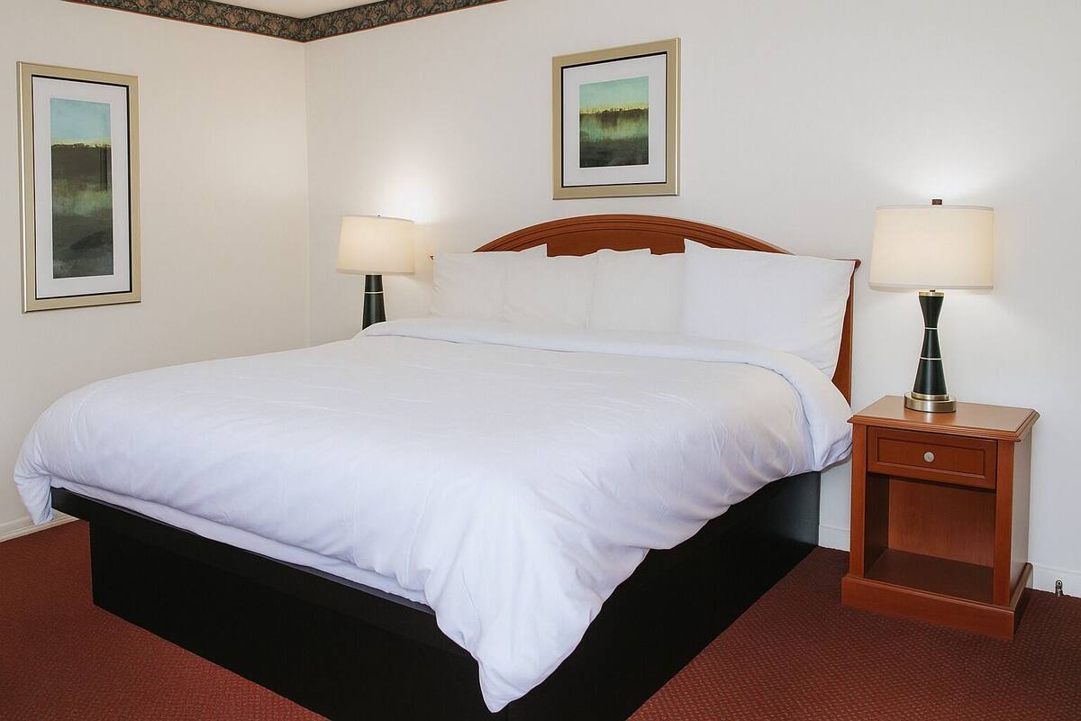 A neatly made bed with white linens, a wooden headboard, and two bedside lamps.