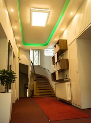 Un interior moderno con una escalera, una alfombra roja y una señal que indica la zona de recepción.