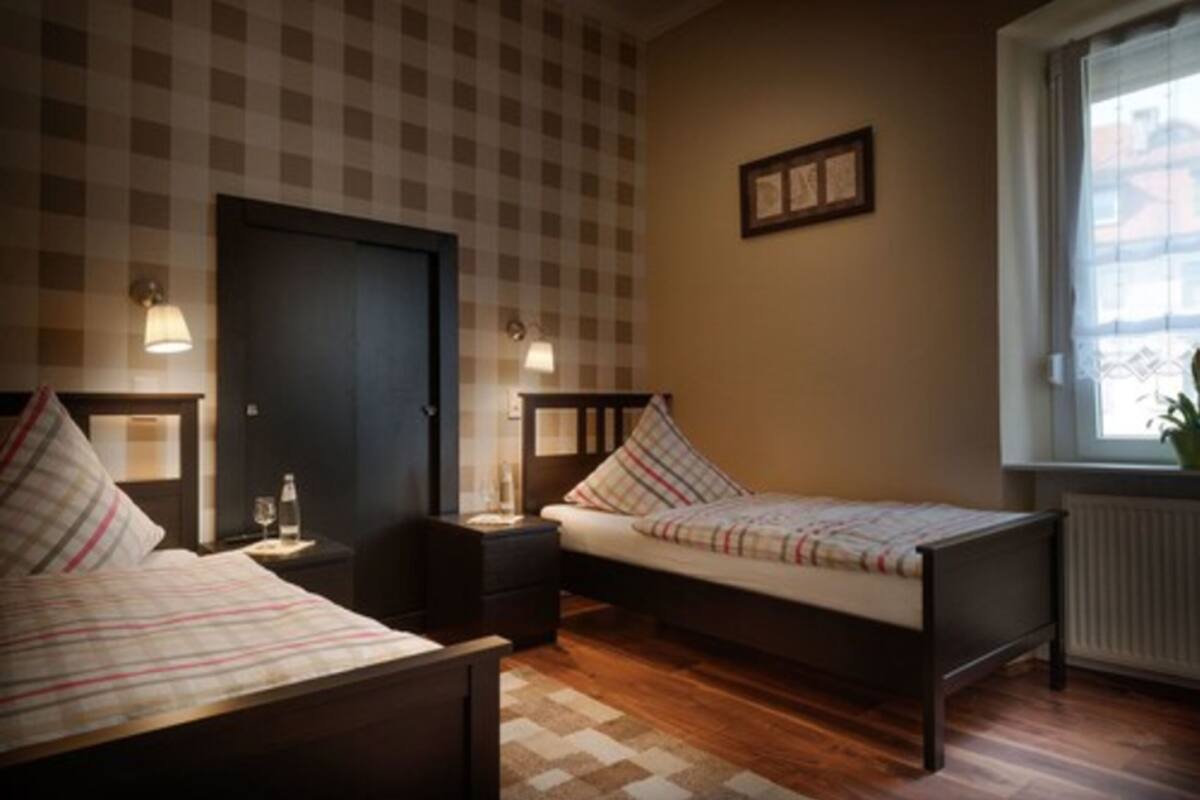 Quarto com duas camas, parede xadrez, quadro emoldurado e janela com planta.