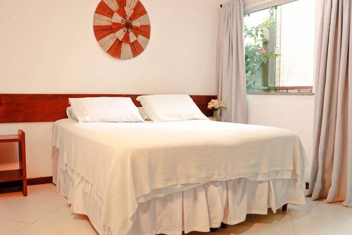 Una cama bien hecha con ropa blanca, un cabecero de madera y un ventilador decorativo fijado a la pared.