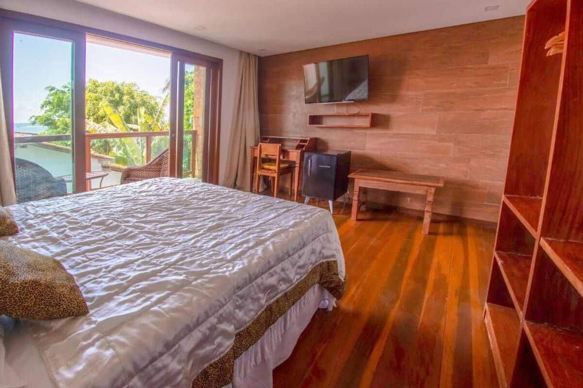 Una habitación de hotel con una cama grande, un televisor montado en la pared, un escritorio de madera y un balcón con vistas al océano.