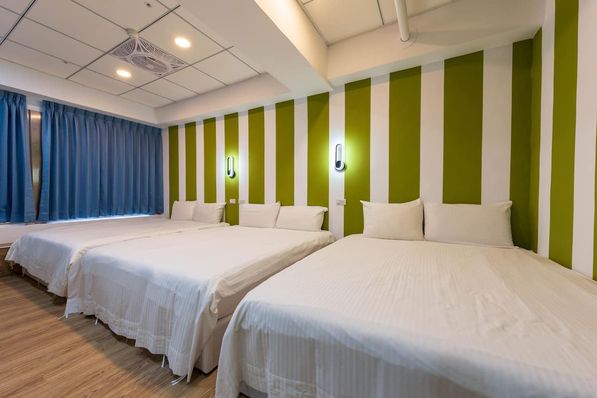A hotel room with three single beds, a large window with blue curtains, and green and white striped walls.