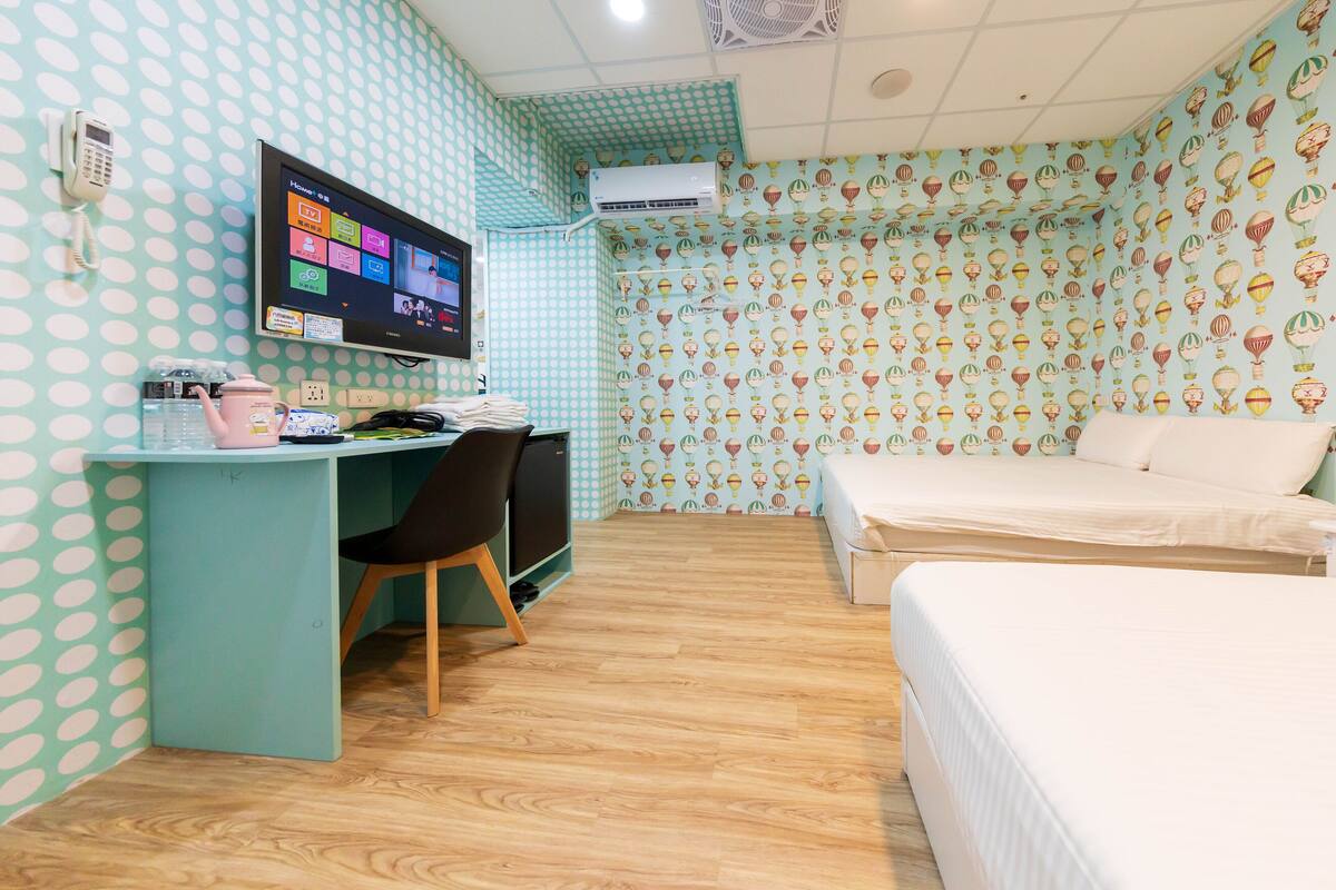 A room with a desk, a bed, a TV, and patterned wallpaper.