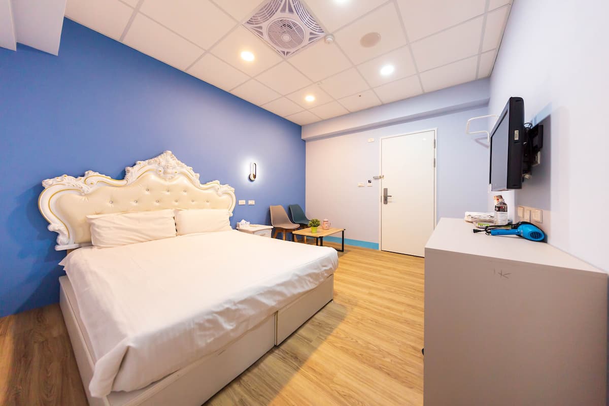 A bedroom with a large bed, a desk, a chair, a TV, and a wardrobe.