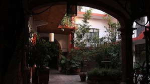 An indoor courtyard with a brick floor, potted plants, and a hanging light fixture. - Cortizo Suites (San Miguel de Allende)