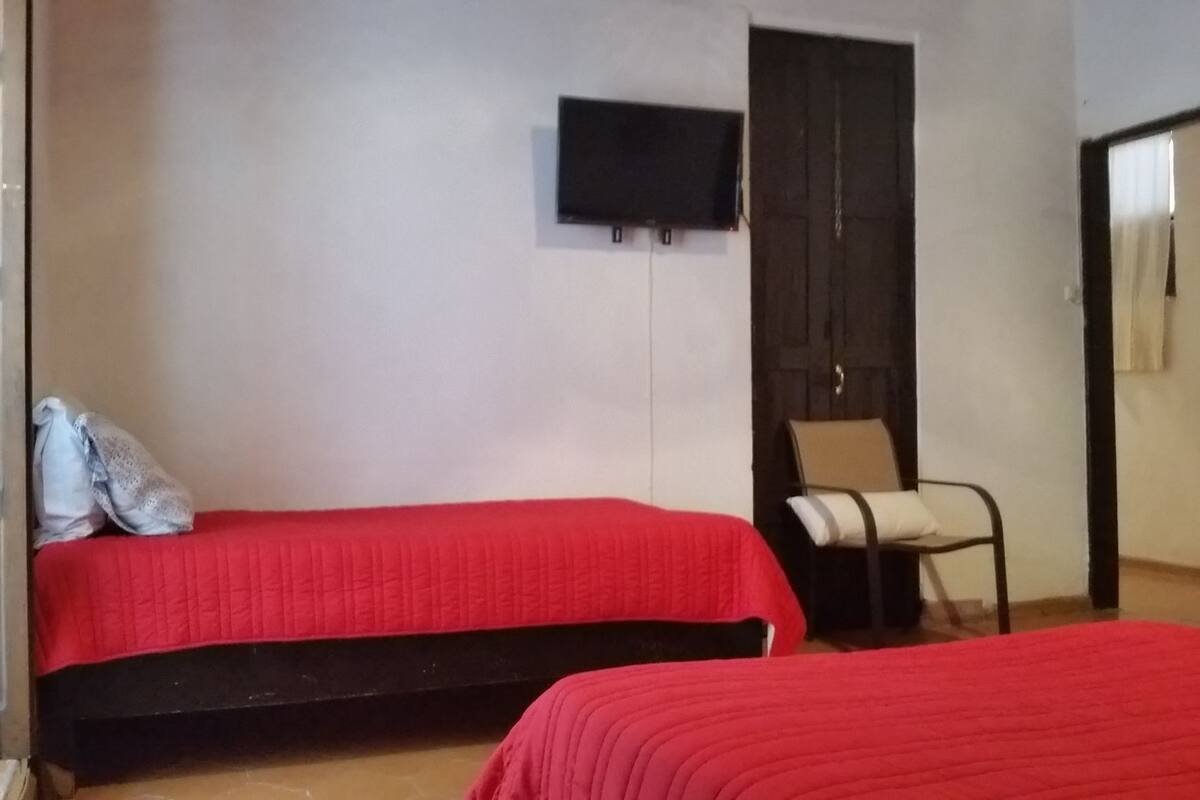 Una habitación con dos camas, televisión en la pared y una silla.