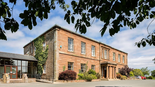 A two-story building with a stone facade, large windows, and a covered entrance. - Greenhill Hotel (Wigton)