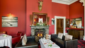 A room with a fireplace, seating, a bar area, and a deer head decoration. - Greenhill Hotel (Wigton)