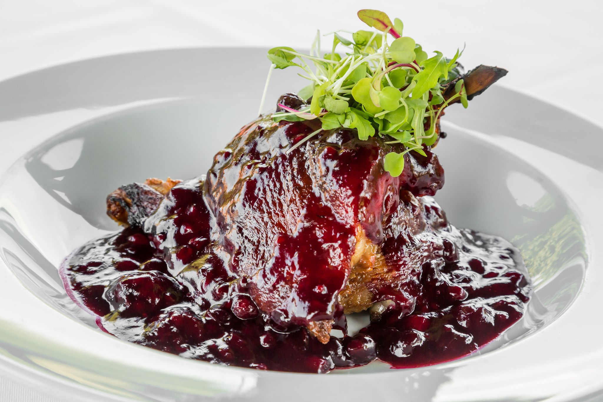 Un plato con salsa de frutos rojos y vegetales verdes.